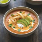 A comforting bowl of creamy taco soup topped with tortilla strips, cheese, and avocado