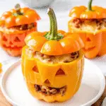 Halloween stuffed peppers carved like Jack-O’Lanterns and filled with rice and meat, served on a festive platter