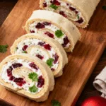 Close-up of sliced Christmas Cranberry Roll Ups showing creamy cranberry and herb filling on a rustic wooden board.