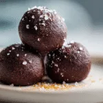 Close-up of three delicious salted chocolate brownie balls on a white plate, showcasing their fudgy texture and sea salt sprinkle.