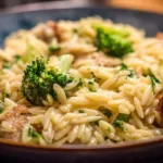 Bowl of creamy orzo with chicken sausage and broccoli garnished with parsley.