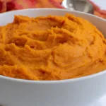 Creamy mashed yams served in a bowl with herbs and spices